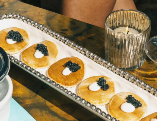 caviar, creme fraiche and blinis on a white and serving tray next to a votive on a brown table