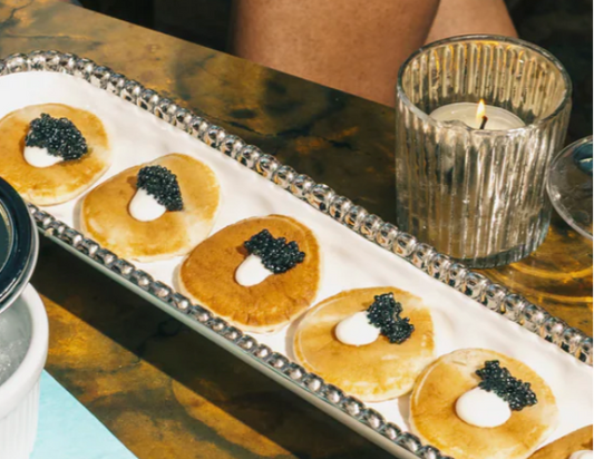 caviar, creme fraiche and blinis on a white and serving tray next to a votive on a brown table