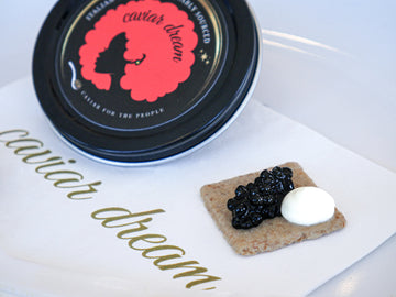 Caviar Dream container with caviar and a dollop of creme fraiche on a cracker.