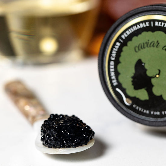Seaweed caviar on a spoon with a caviar jar and glass of white wine in the background