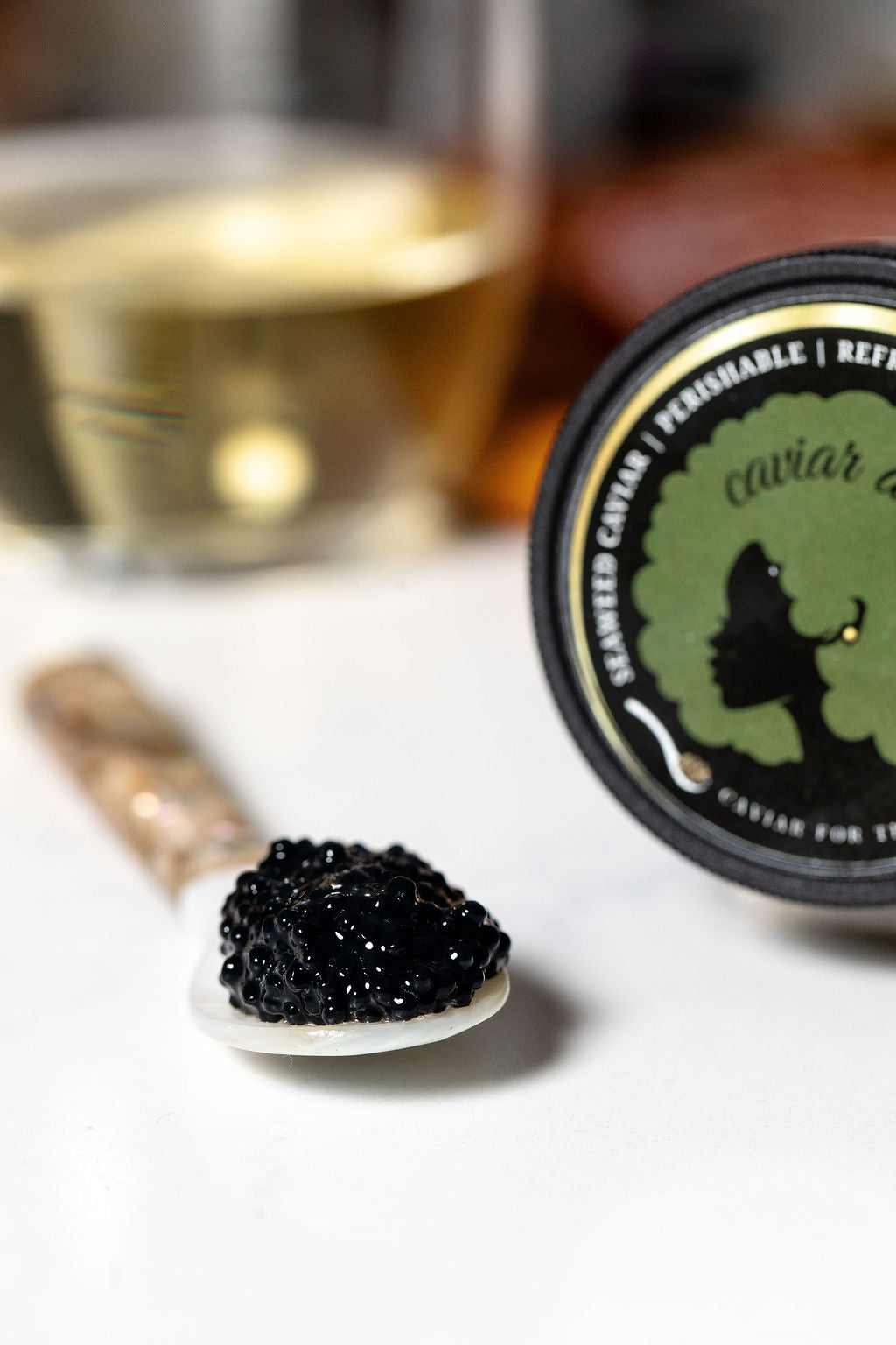 Seaweed caviar on a spoon with a caviar jar and glass of white wine in the background