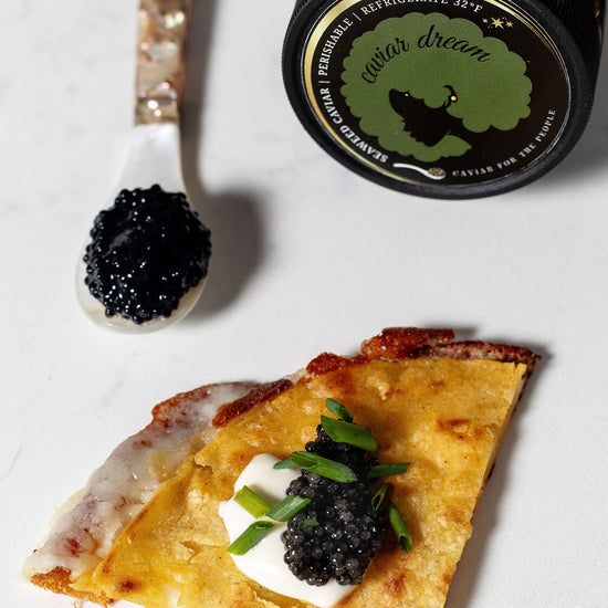 Quesadilla small bite with caviar and a jar labeled 'Caviar Dream' on a white surface. Top left has a spoon with eaweed ccaviar on it.
