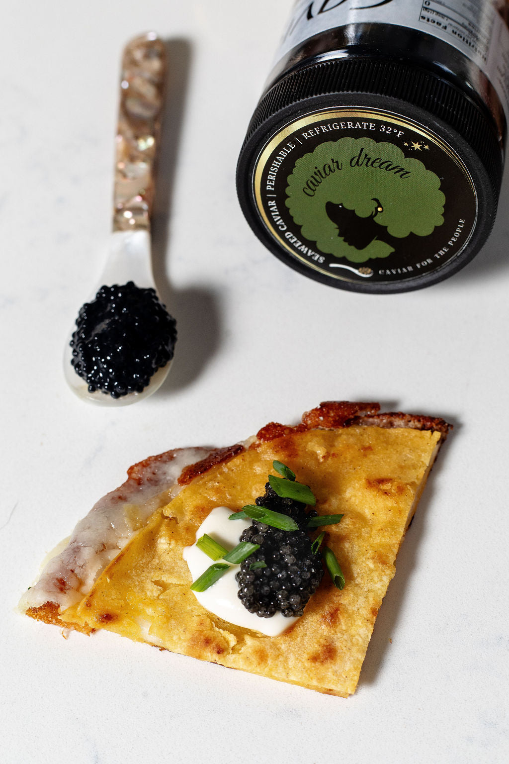 Quesadilla small bite with caviar and a jar labeled 'Caviar Dream' on a white surface. Top left has a spoon with eaweed ccaviar on it.