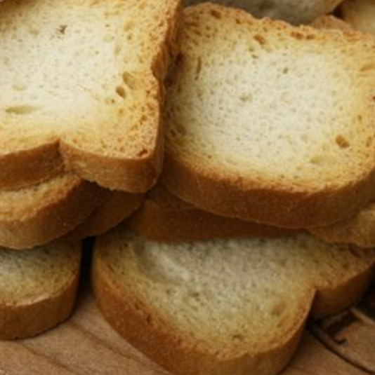 A pile of golden-brown mini toasts on a wooden surface.